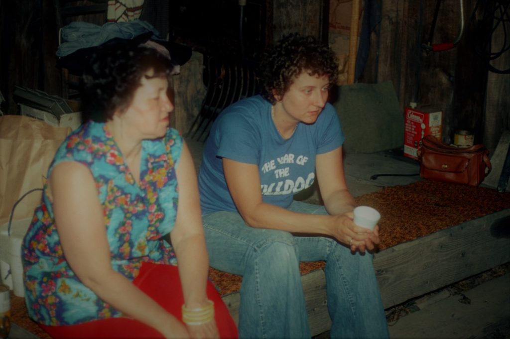 marie harned and becky harned wearing blue t shirt "year of the bulldog' seated in cabin in cortland circa 1980